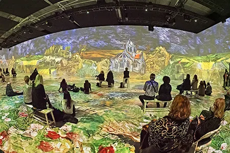 Người xem ngồi rải rác trong một gian triển lãm, tranh Van Gogh được chiếu phủ kín cả tường lẫn sàn.